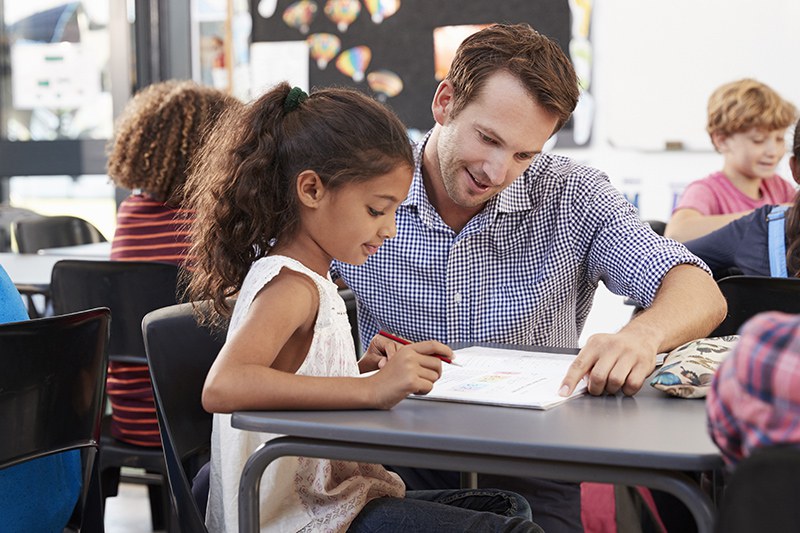 Primarlehrer im Klassenzimmer mit Schülerin - Studium an der PH Zugeit