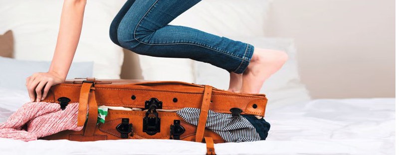 Frau versucht Koffer zu schliessen, der mit Kleidern überquillt